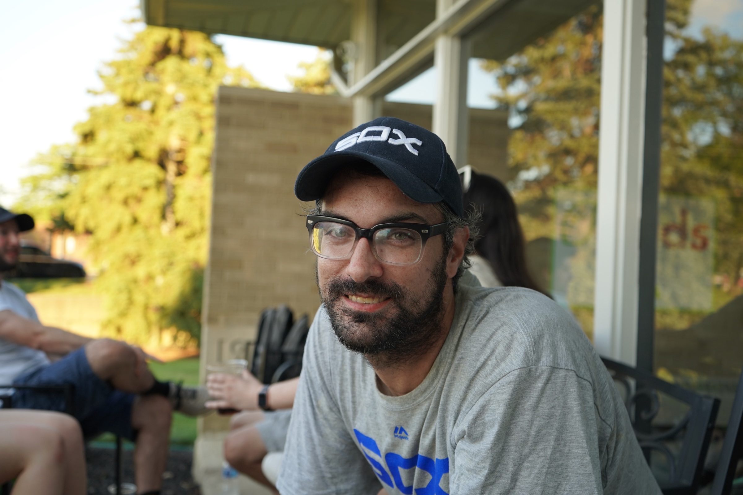 Young man with glasses and a dark cap seated outdoors
